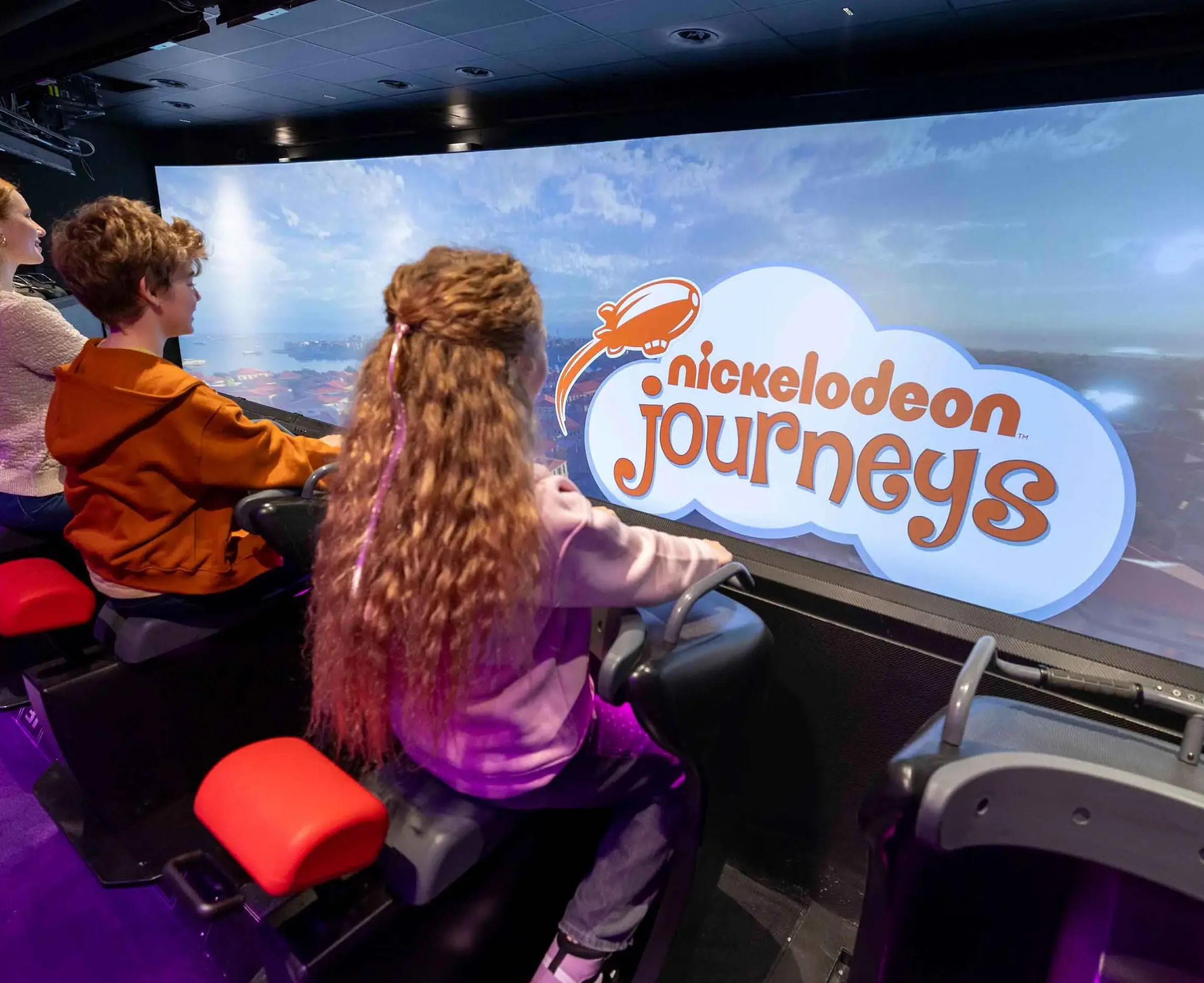 Çocuklar Nickelodeon Journeys oyuncağı önünde koltuklarda oturuyor ve ekrana bakıyor.